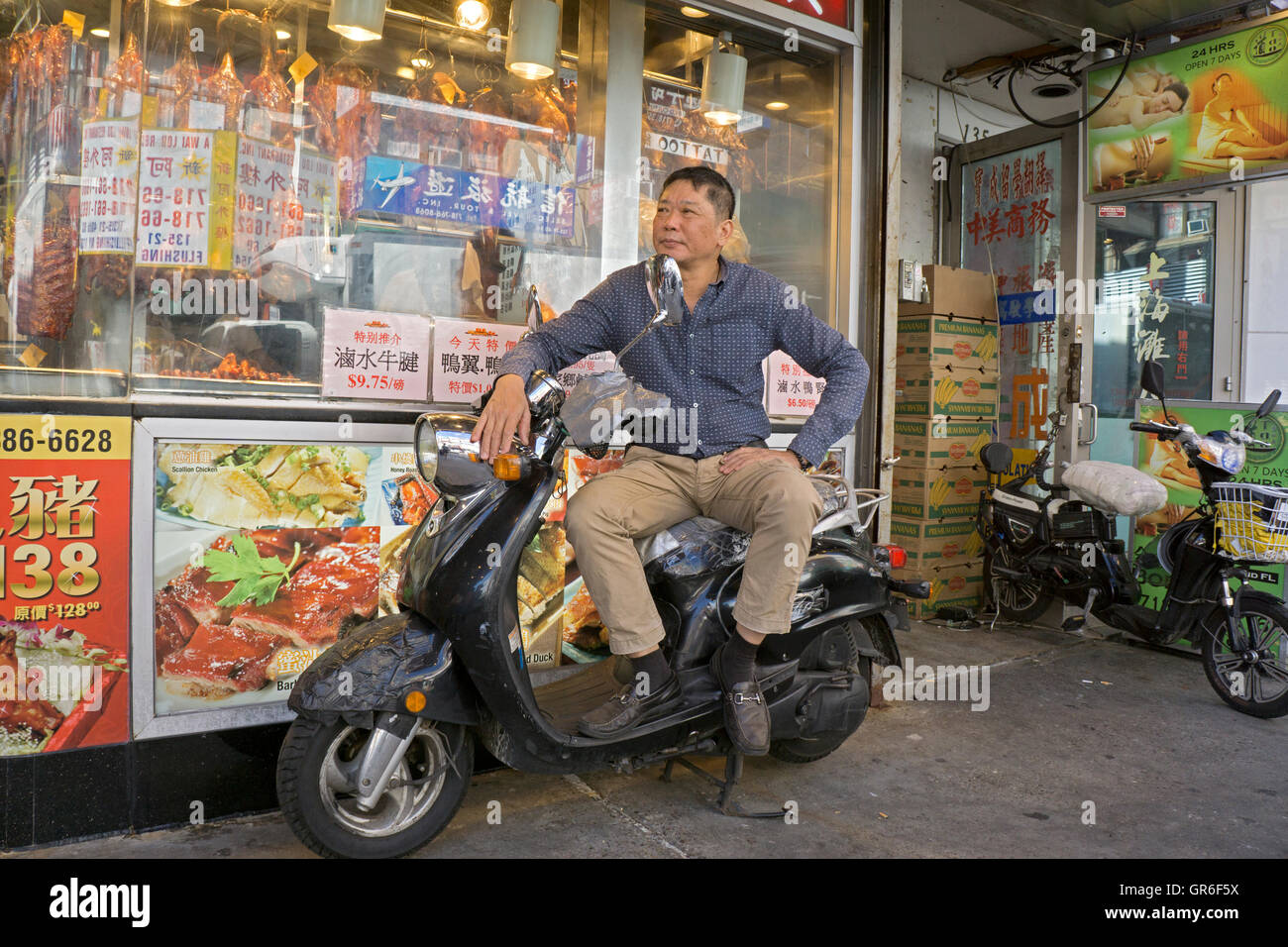 Porträt einer asiatisch-amerikanische Mann sitzt auf einem Zusteller Roller vor einem Restaurant in Downtown Flushing, Queens, New York. Stockfoto