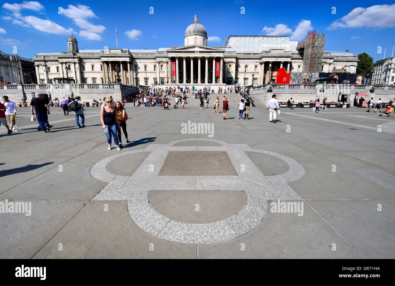London, England, Vereinigtes Königreich. Trafalgar Square. National Gallery (Hintergrund) und Plaque im Pflaster unter Bezugnahme auf den Brunnen und... Stockfoto