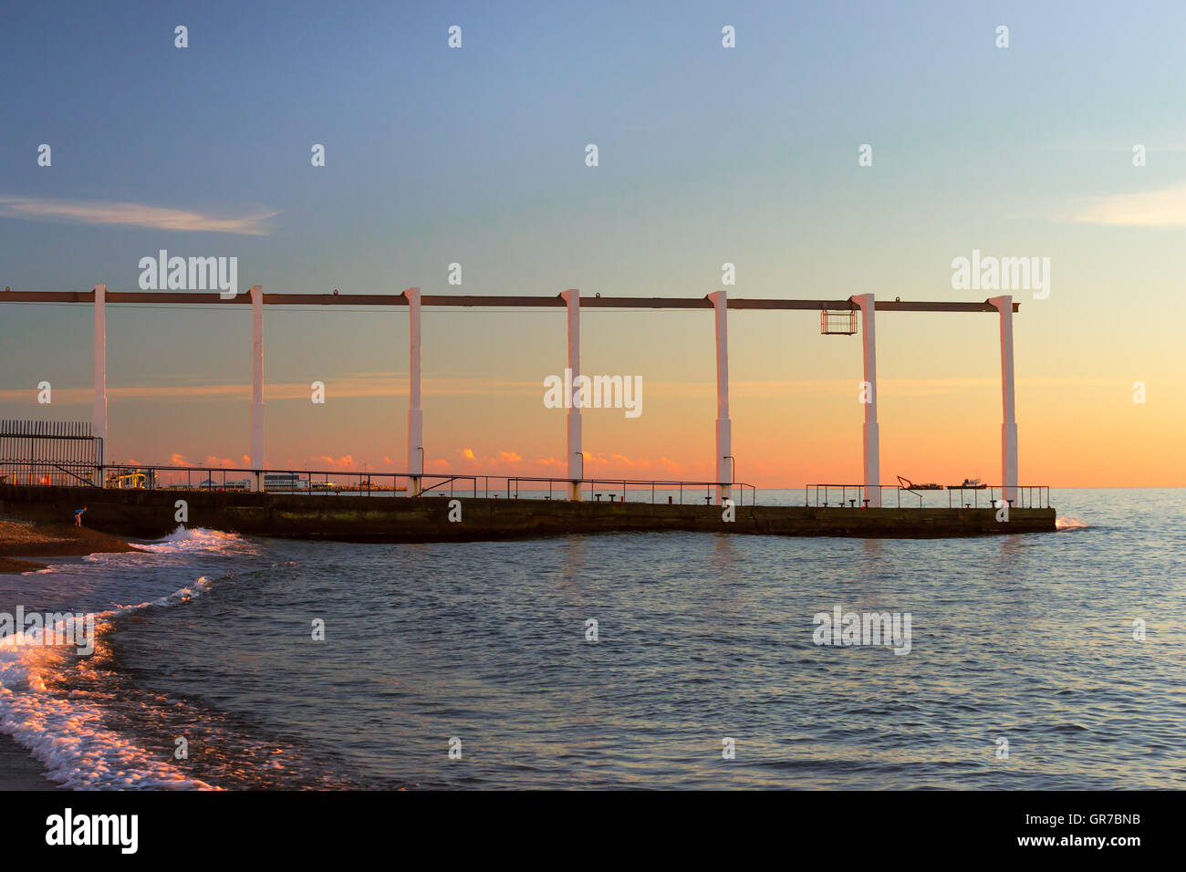 Betonpfeiler mit einer Transport-Schiene oben am Meer, die Wellen zu versinken. Sonnenuntergang am Strand am Schwarzen Meer im Oktober. Sotschi Stockfoto