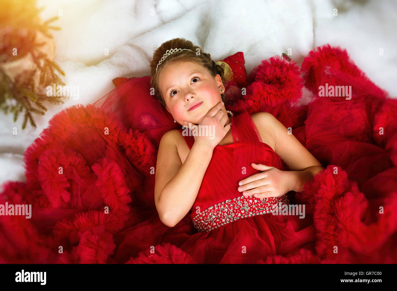 Kleines Winter Prinzessin in eine kostbare Krone im roten Kleid liegt auf Kunstschnee. Begrüßt, Weihnachten und Neujahr Stockfoto