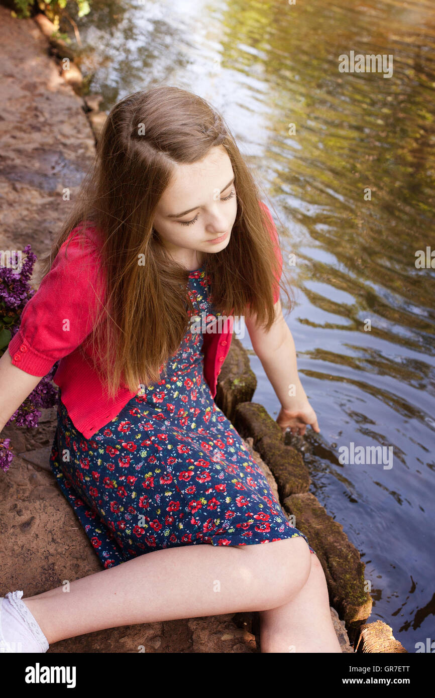 Schöne Teenager-Mädchen sitzt neben einem Fluss und ihre Hände ins Wasser tauchen Stockfoto