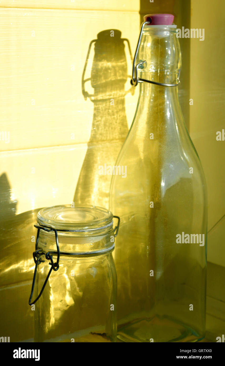 Glasflasche und Glas mit Schatten auf gelbem Hintergrund. Stockfoto