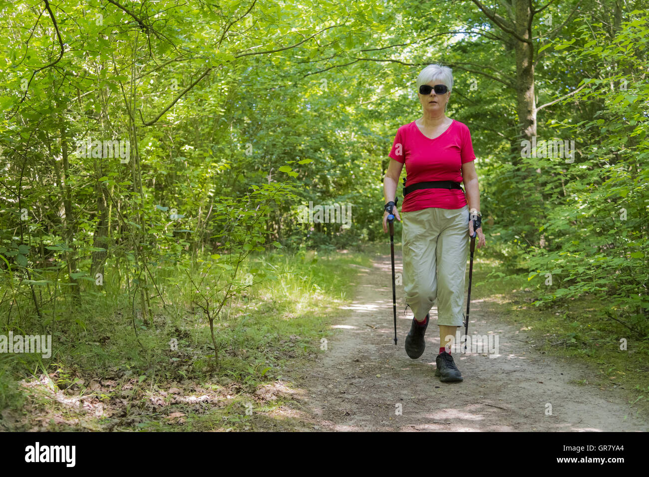 Eine ältere Dame im Sport Nordic Walking auf einem Waldweg. Stockfoto