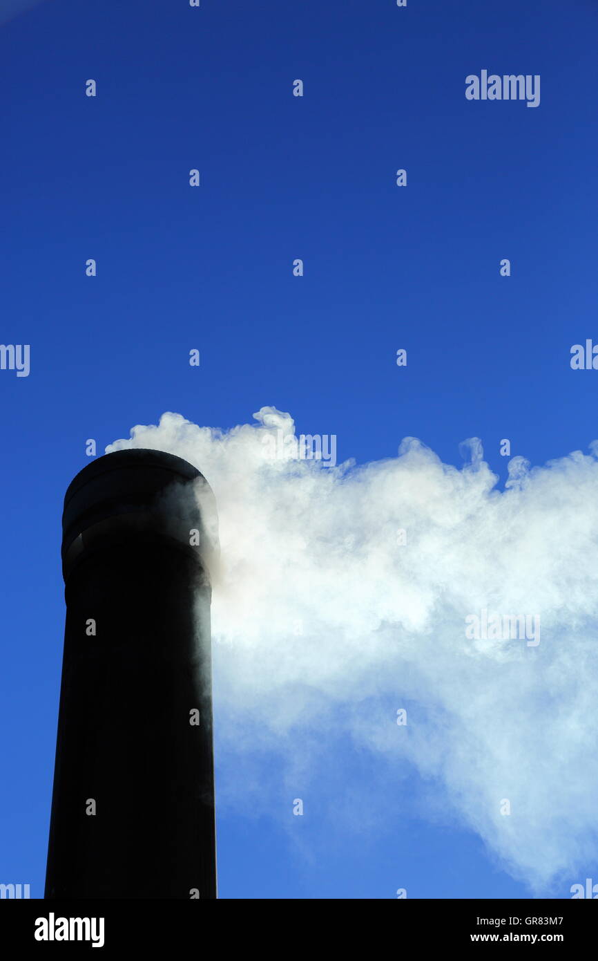 Rauch strömt aus einem Schornstein unter einem pulsierenden klaren blauen Himmel. CO2-Emissionen stehen ganz oben auf aktuelle Themen Bezug auf den Klimawandel Stockfoto