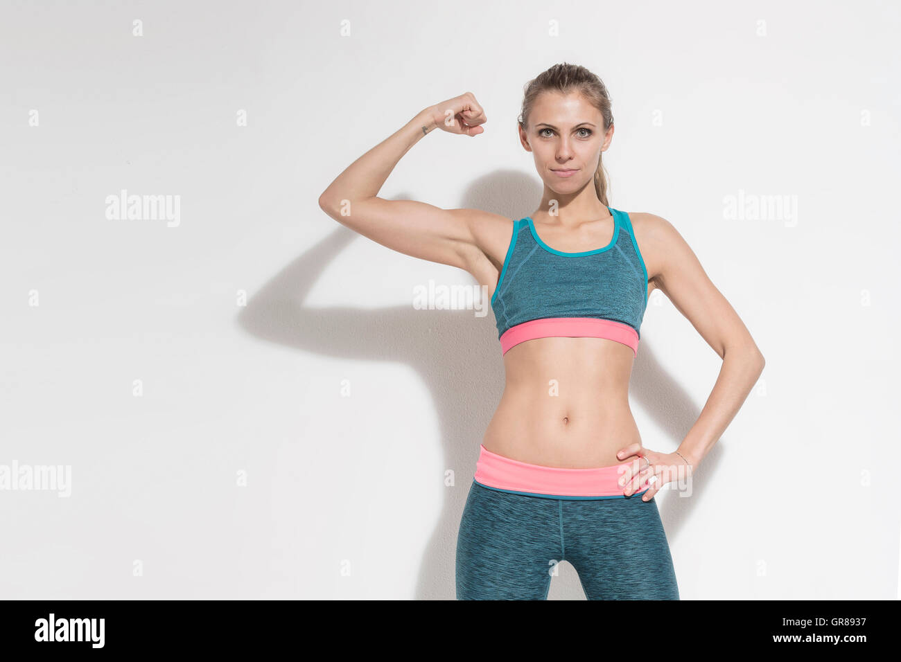 Junge Frau mit einem sportlichen Outfit zeigt dem Betrachter ihre Muskeln Stockfoto