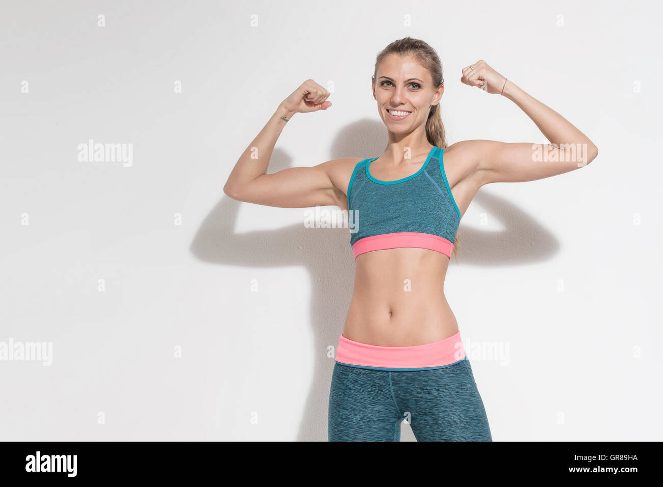 Junge Frau mit einem sportlichen Outfit zeigt dem Betrachter ihre Muskeln Stockfoto