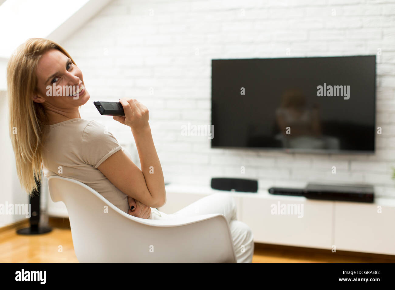 Frau mit einer TV-Fernbedienung im Wohnzimmer sitzen Stockfoto
