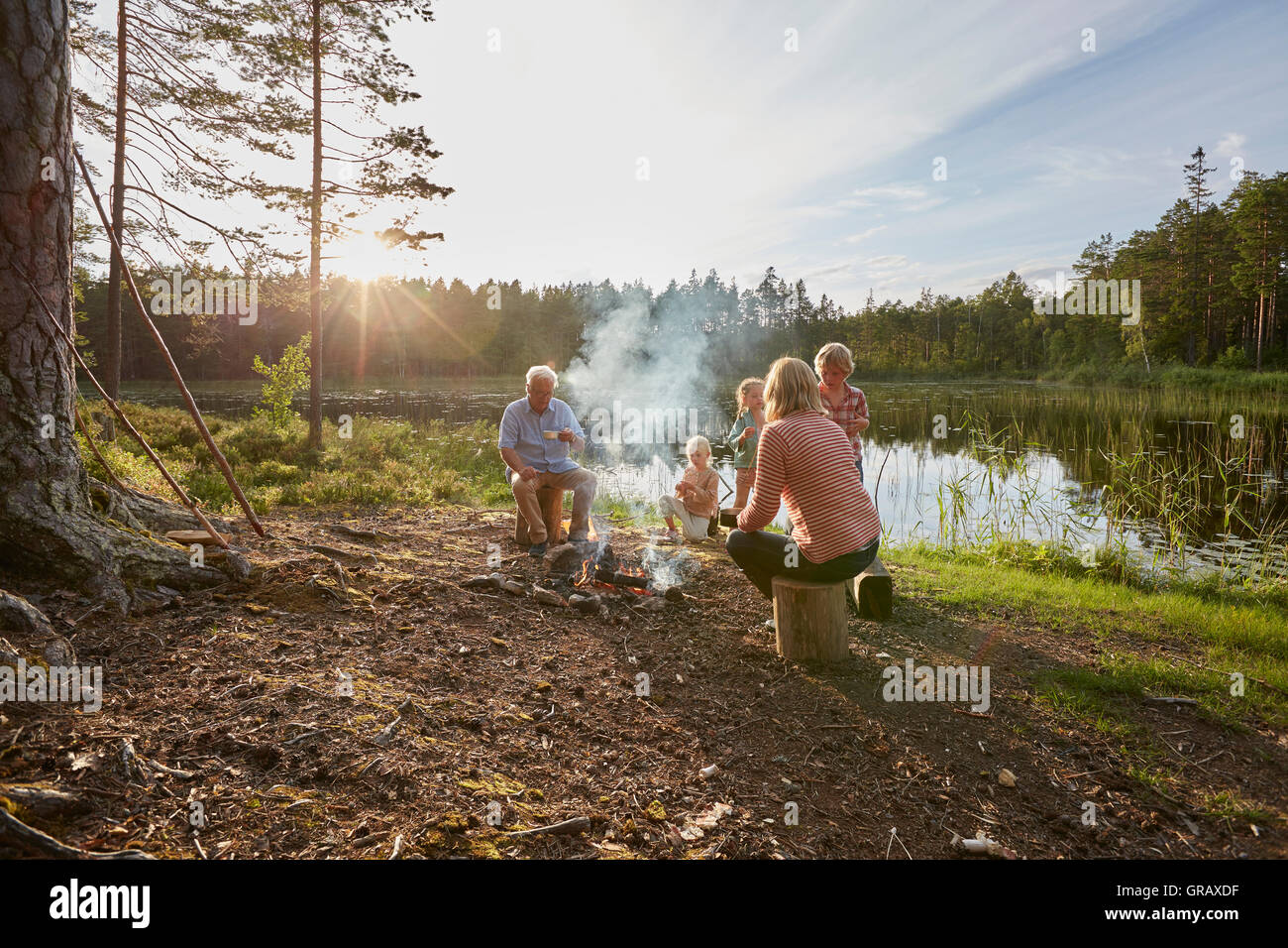 Großeltern und Enkelkinder Lagerfeuer am sonnigen Seeufer in Wäldern genießen Stockfoto