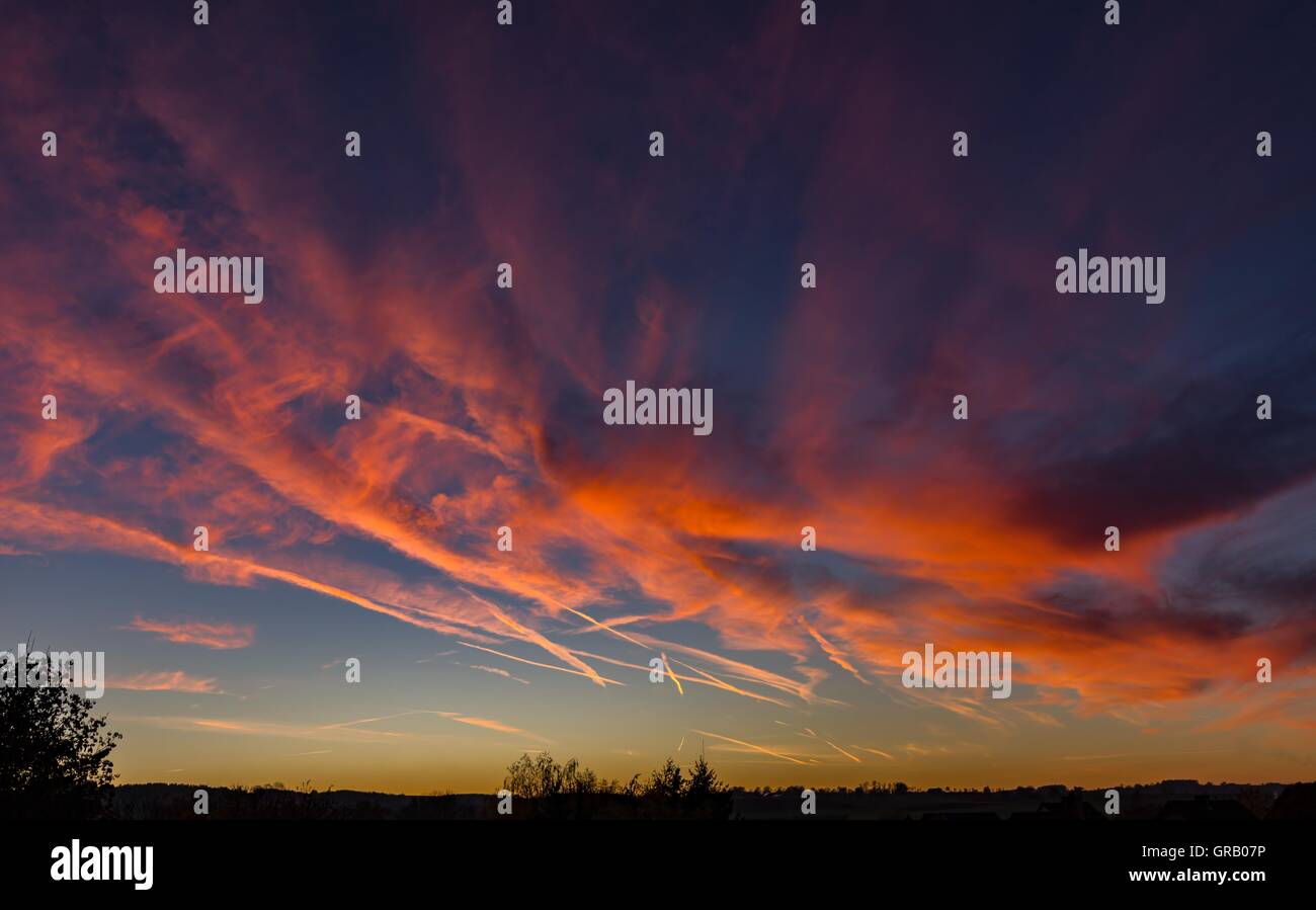 Dramatische Wolkenformation bei Sonnenuntergang mit vielen Kondensstreifen Stockfoto