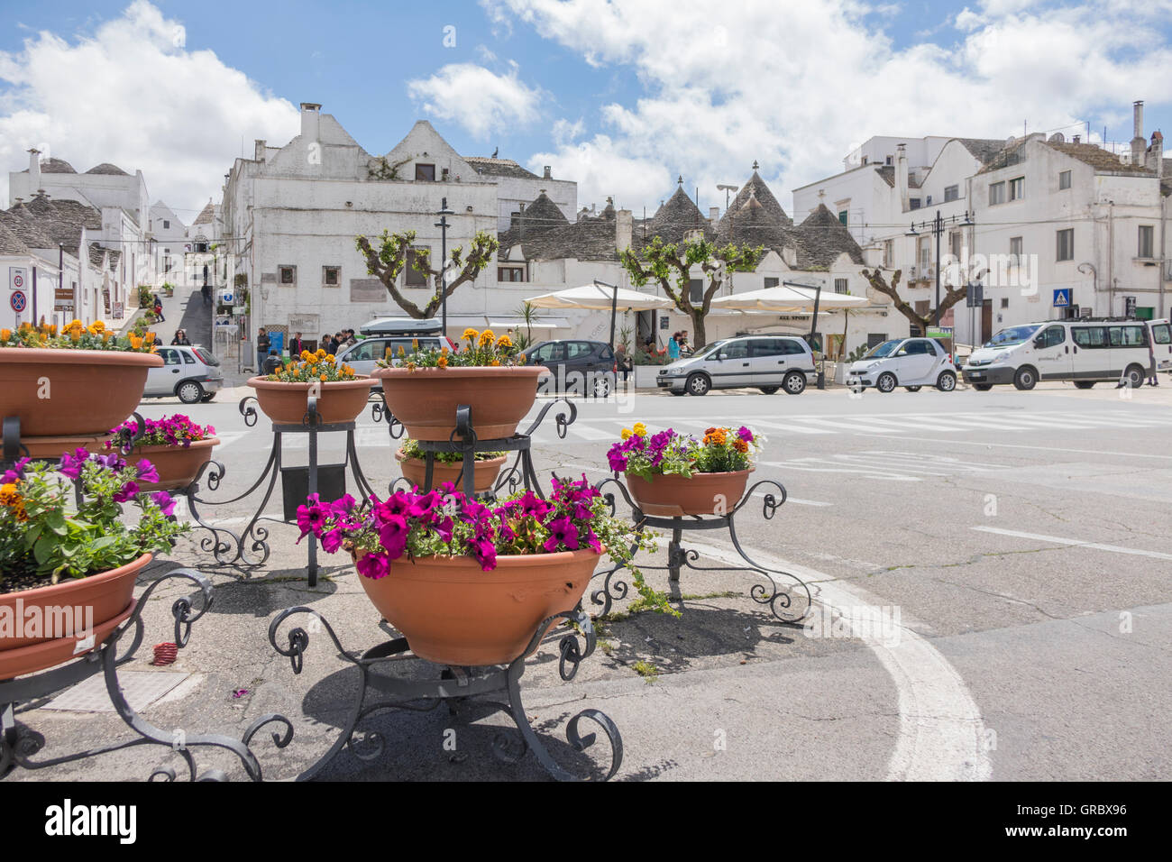 Blumentöpfe In den Vordergrund, alten Teil der Stadt, Trulli, im Hintergrund. Blauer Himmel, weiße Wolken. Largo Martellotta, Alberobello, Provinz Bari, Apulien, Italien Stockfoto