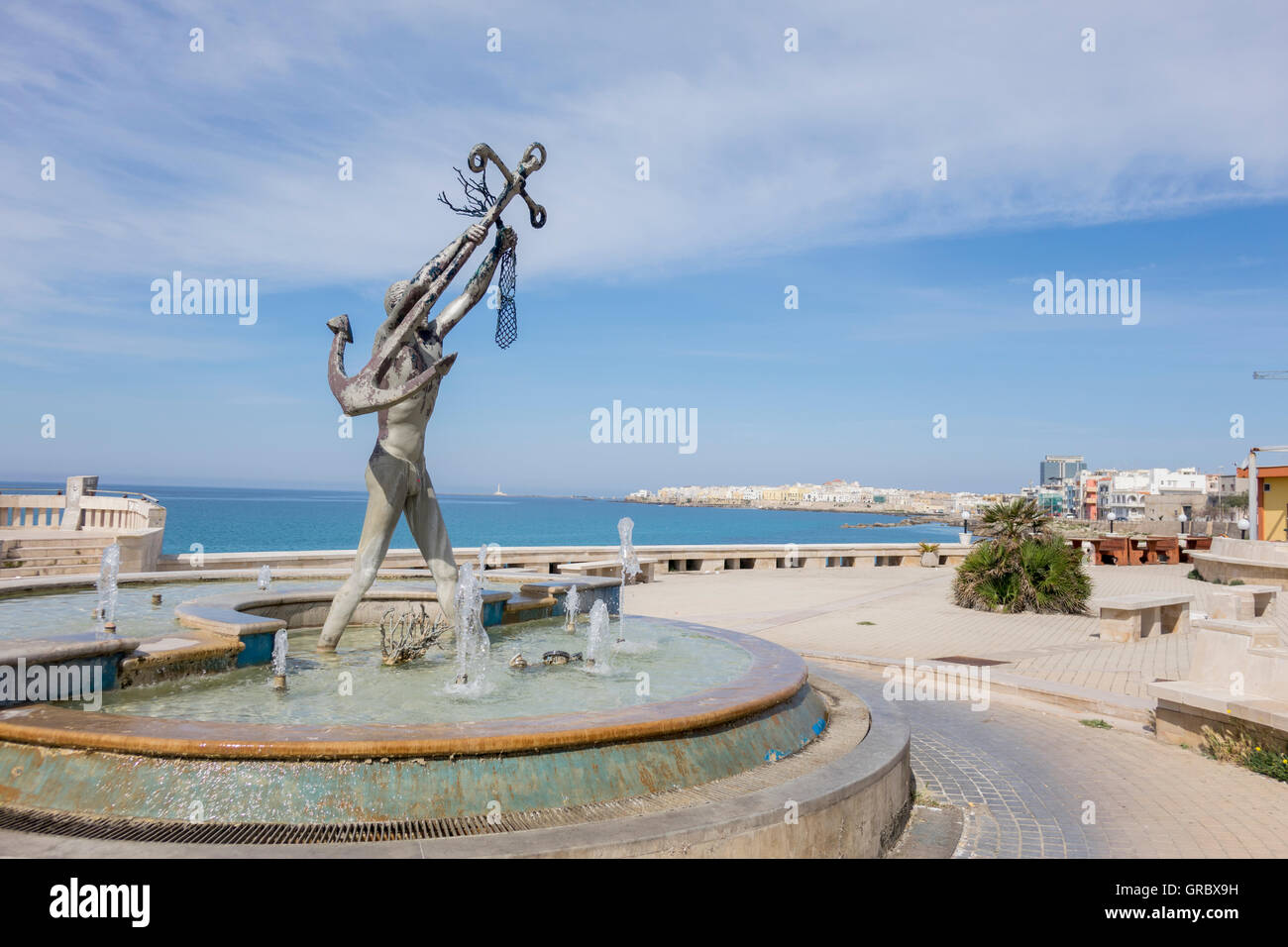 Im Vordergrund ein Brunnen mit einer Sailor Skulptur hält einen Anker im Hintergrund Golf von Tarent und Gallipoli Stockfoto