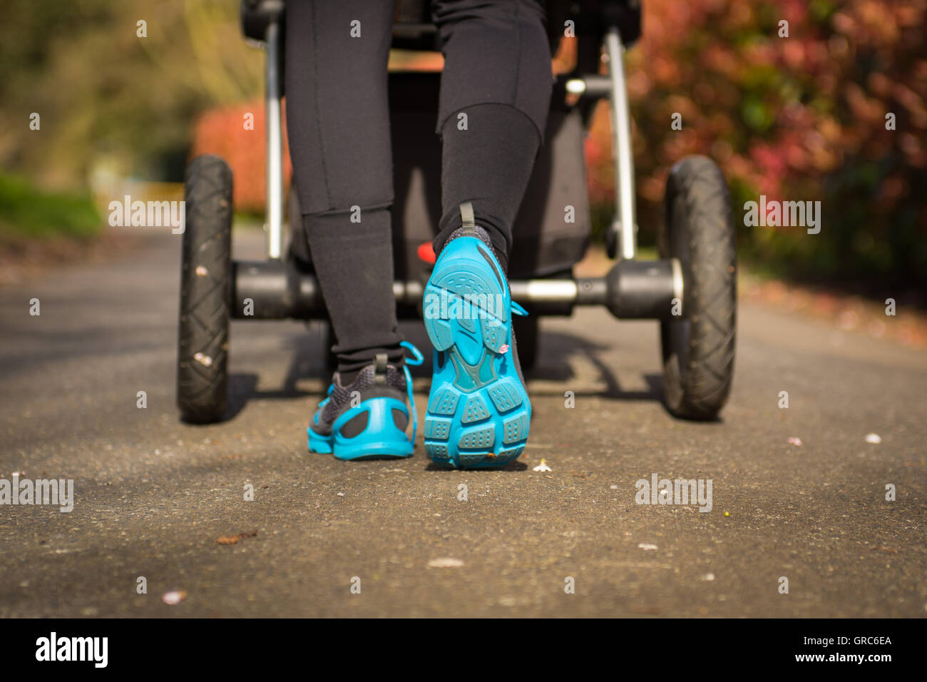 Junge Mutter Übungen in einem Park. Blau-grau Sportschuhe trägt, schiebt einen Kinderwagen Stockfoto