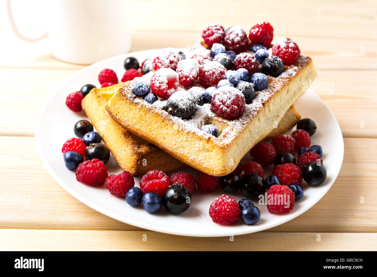 Frühstück Waffeln mit frischen Beeren und Kaffeetasse. Weiche belgische Waffeln mit Heidelbeeren, Himbeeren und schwarzen Johannisbeeren. Stockfoto