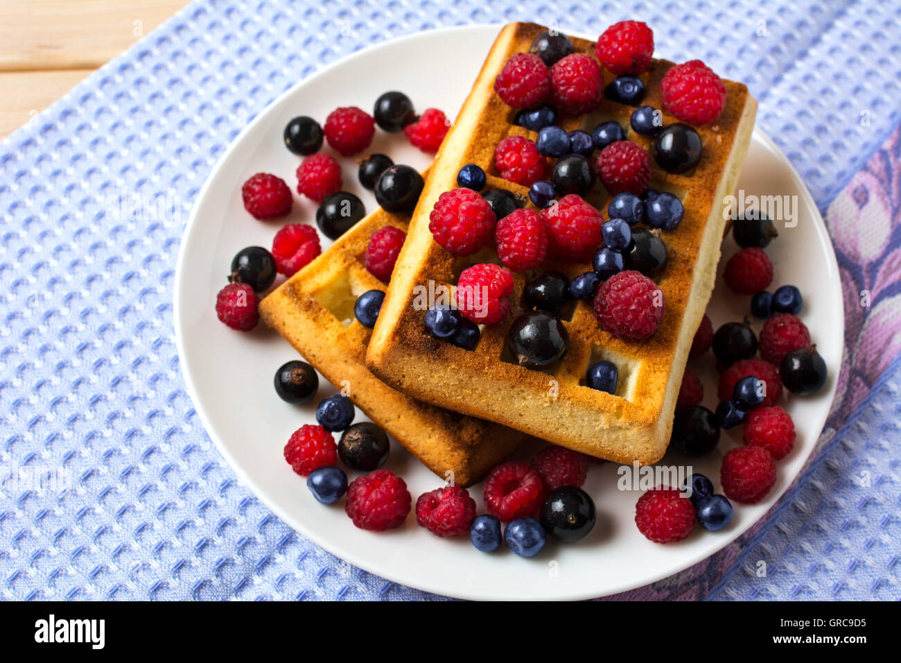 Frühstück Waffeln mit frischen Beeren auf der blauen Leinen-Serviette. Weiche belgische Waffeln mit Heidelbeeren, Himbeeren und schwarzen Johannisbeeren. Stockfoto