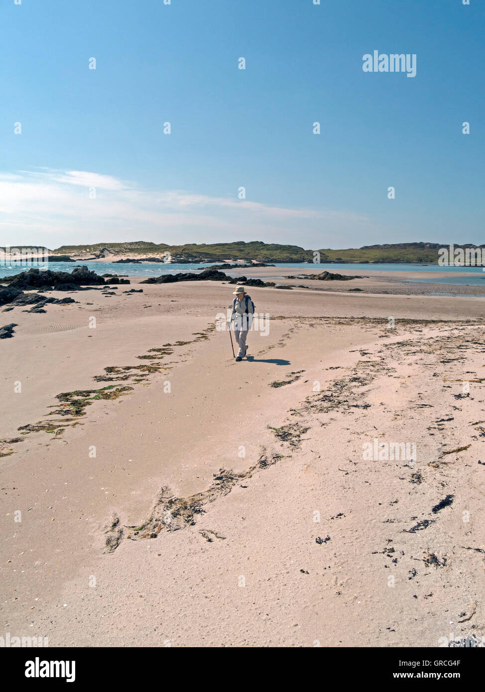 Frau zu Fuß auf der sandigen Strand von The Strand auf Insel Colonsay, mit der Insel Oronsay auf Distanz, Schottland, UK. Stockfoto