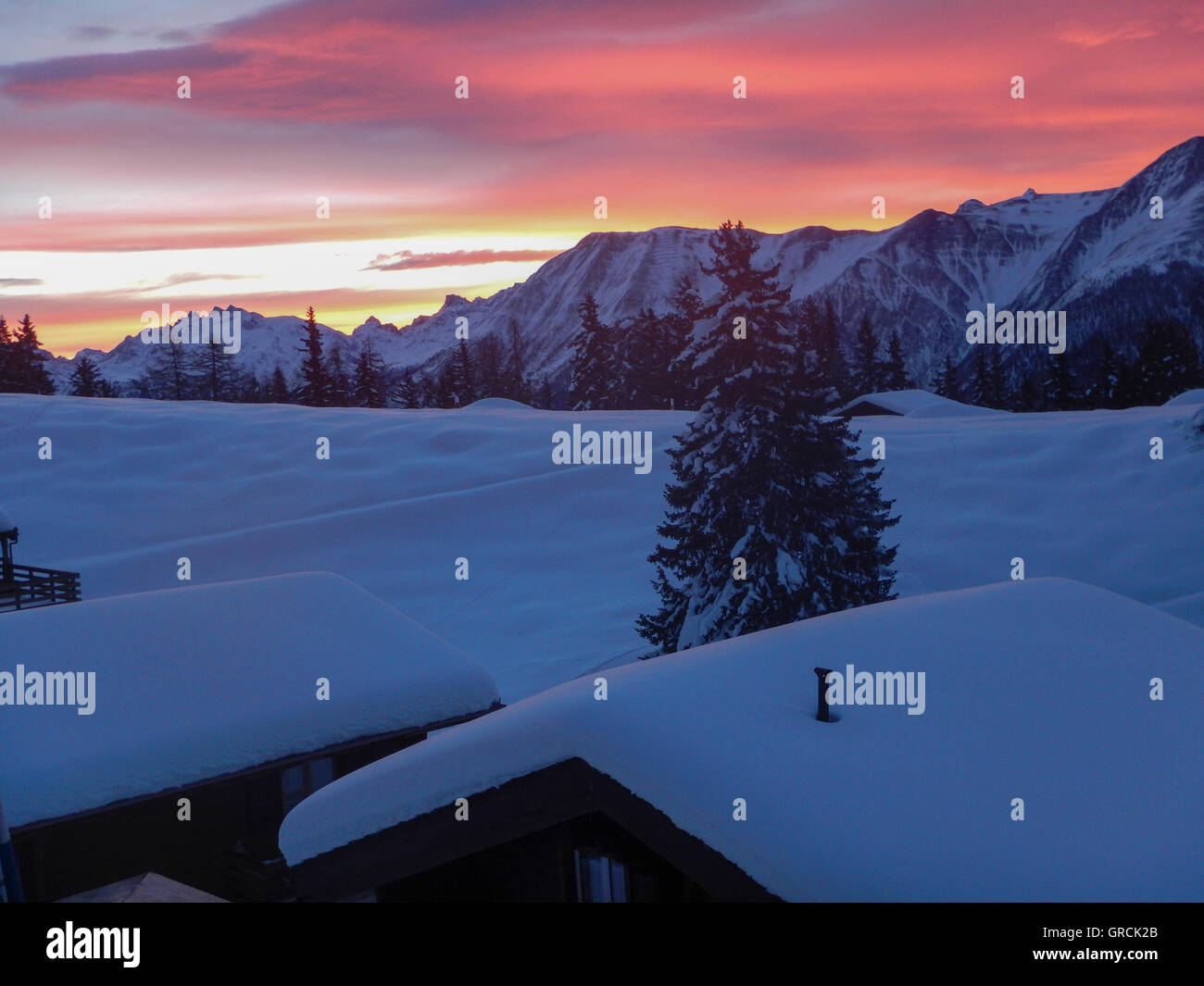 Dawn. Blick über schneebedeckte Dächer der Chalets in die Berge. Sky Orange rosa gefärbt Stockfoto