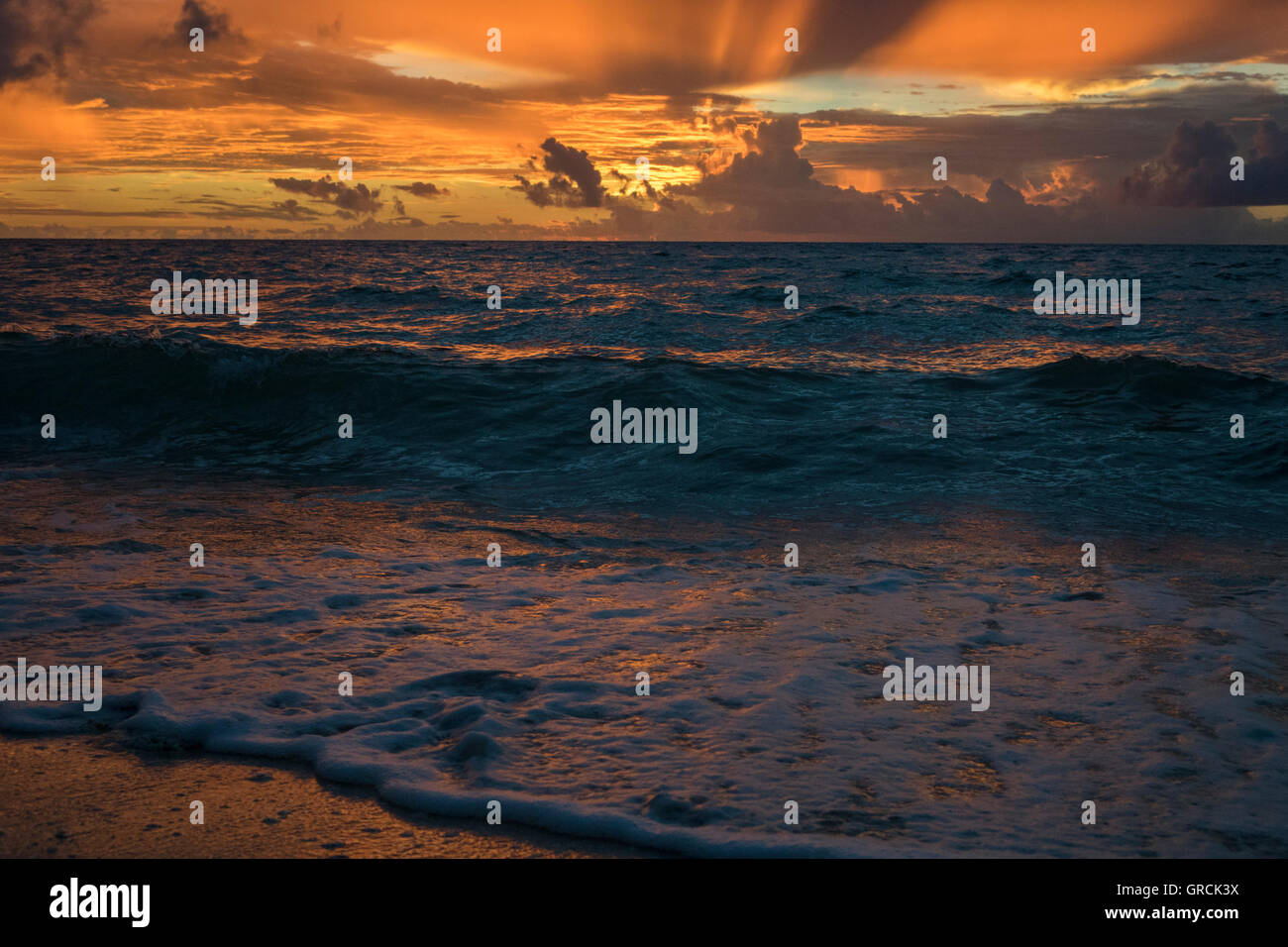 Wellen im Sandy Beach im Morgengrauen, Wolken In Orange Licht Stockfoto