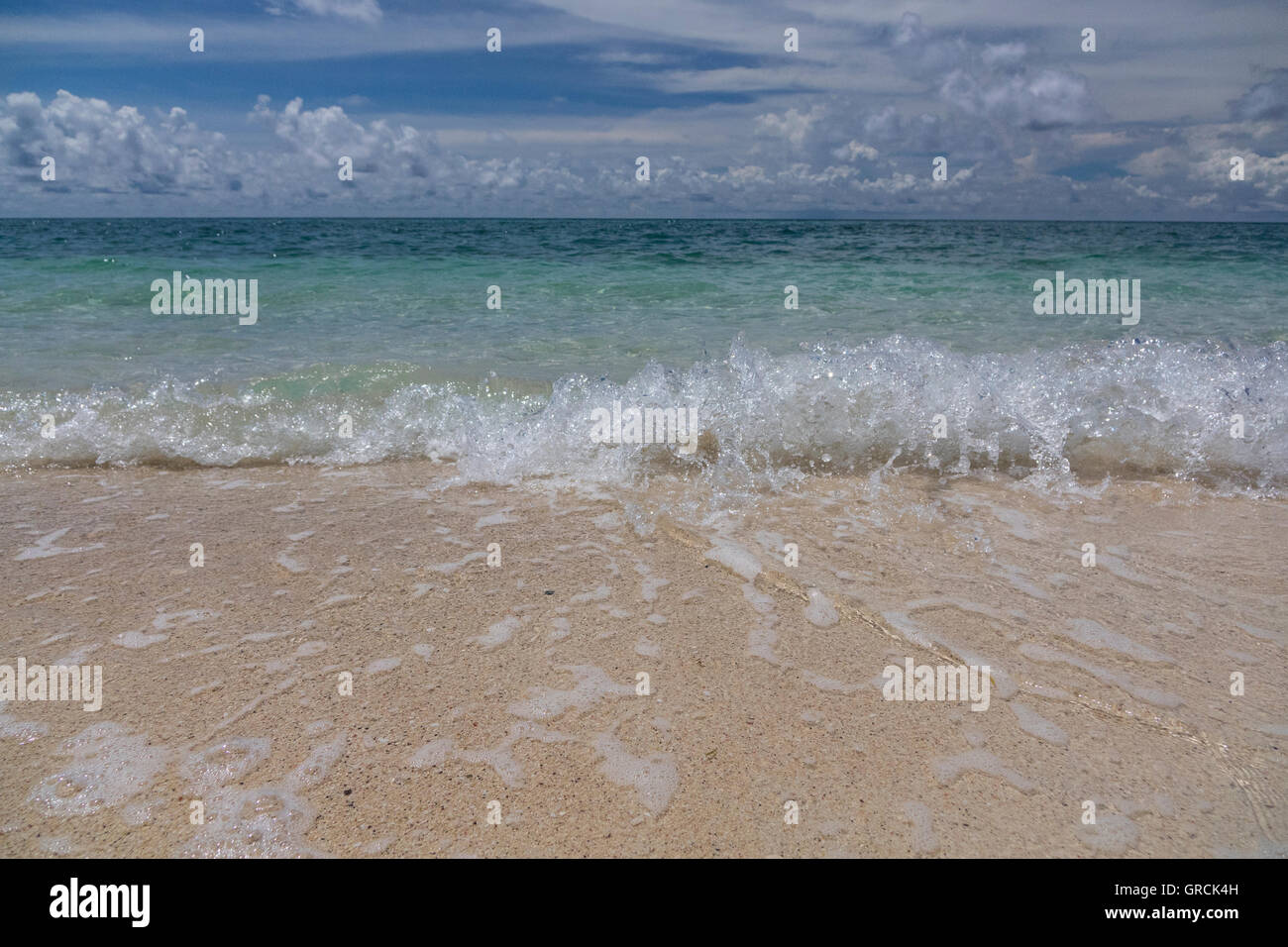 Kleinen plätschernden Wellen auf einen weißen Sandstrand. Blauen Himmel, weiße Wolken Hintergrund Stockfoto