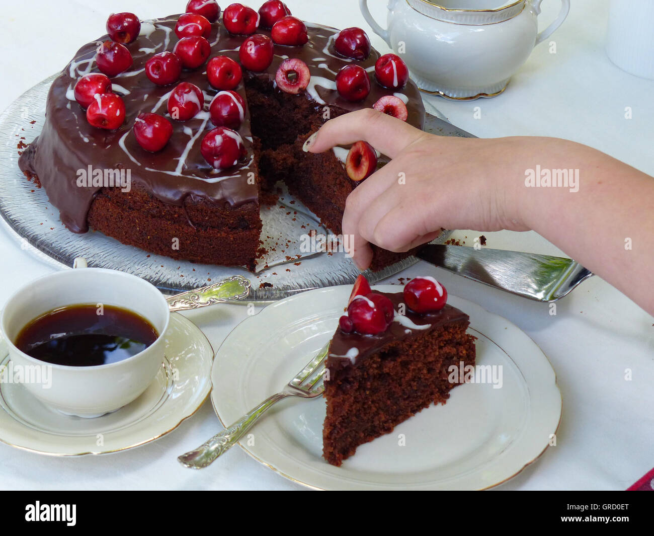 Kirschkuchen auf einem Couchtisch, eine Hand eines Kindes nimmt ein Stück Kuchen Stockfoto