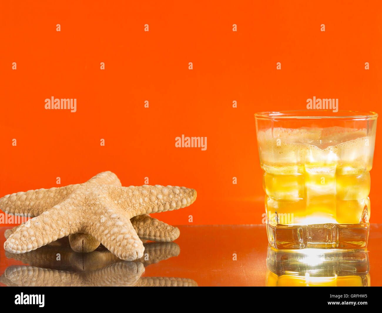 Sommerdrink und ein Seestern gegen einem orangefarbenen Hintergrund Stockfoto