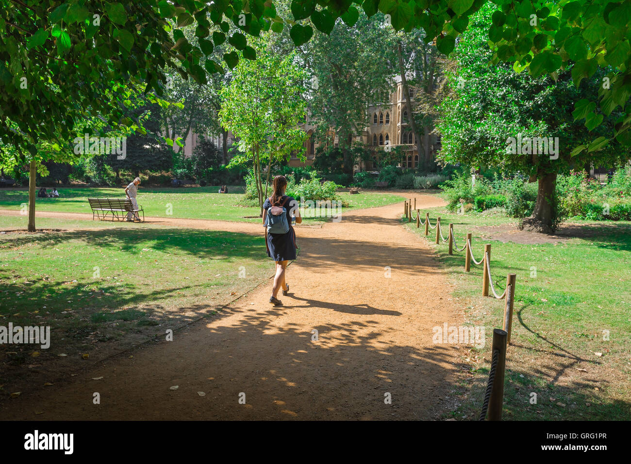 Junge Frau parkt, Rückansicht einer jungen Frau, die einen Rucksack trägt und an einem Sommertag durch den Gordon Square in Bloomsbury, London, Großbritannien, läuft. Stockfoto