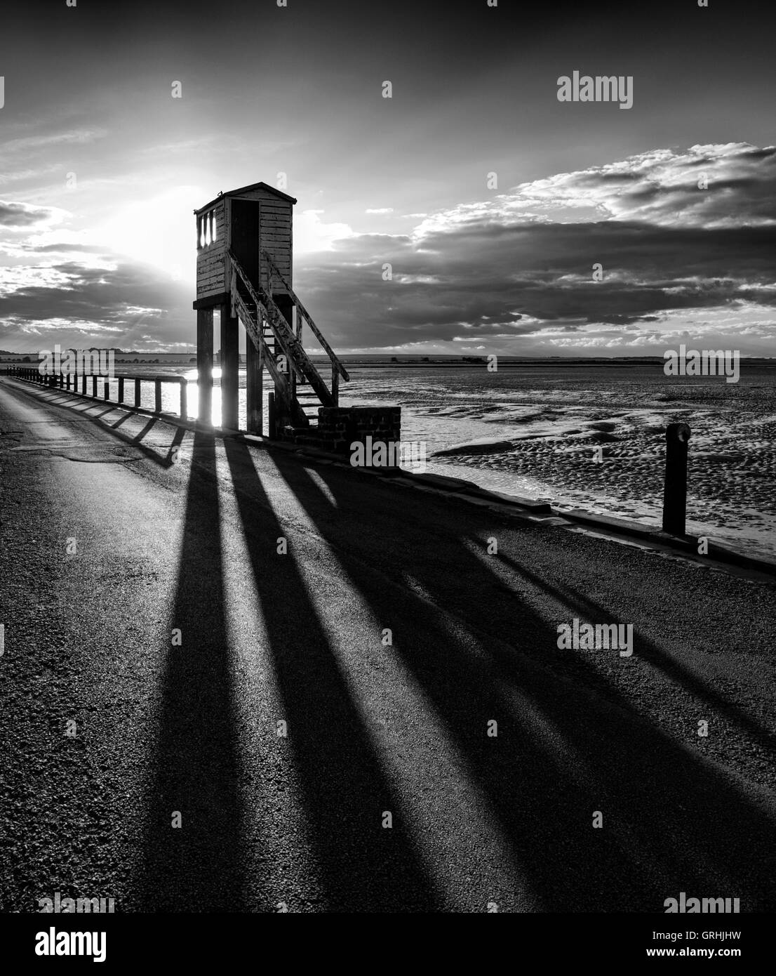 Hinterleuchtete niedrige Sonne wirft Schatten aus dem Notruf-Uhr-Turm auf dem Damm auf der Heiligen Insel, Northumberland England UK Stockfoto