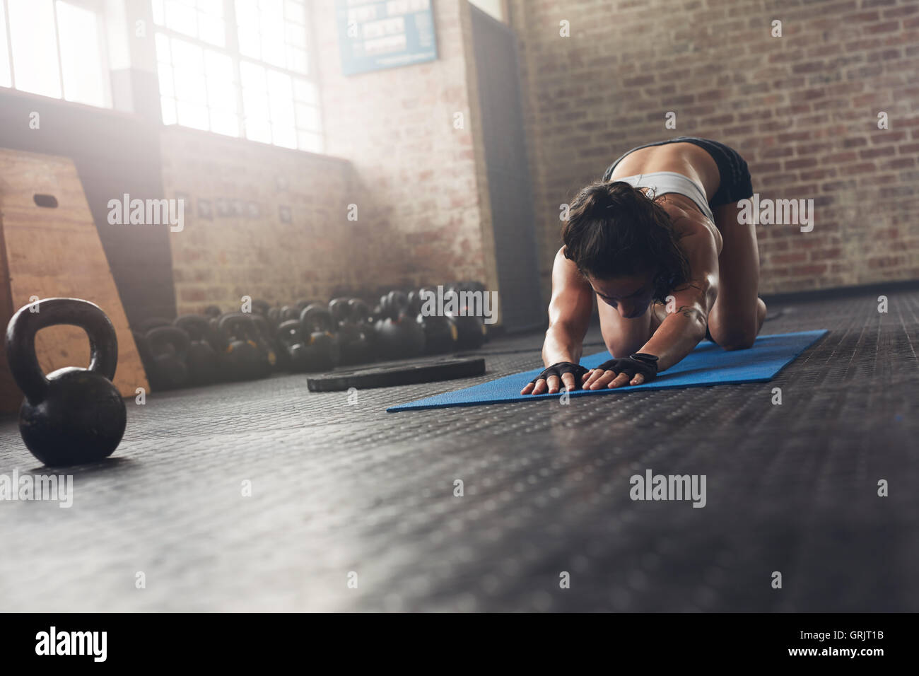 Junge Frau dabei stretching Training in einem Fitnessclub. Frau an Gymnastikmatte erstreckt sich dabei im Fitnessstudio. Stockfoto