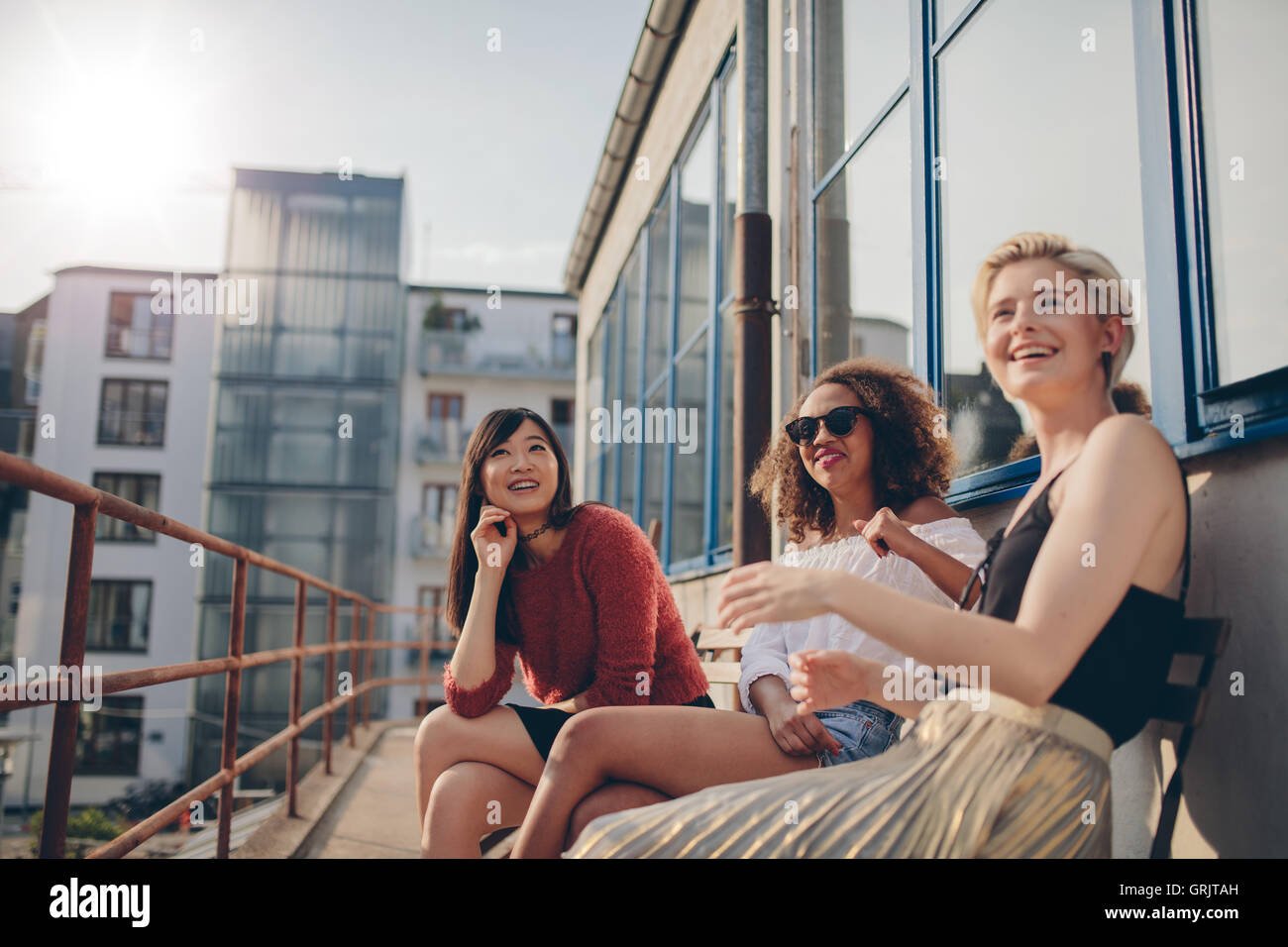 Glücklich drei jungen Freundinnen im Balkon sitzen und Lächeln auf den Lippen. Frauen im Freien auf der Terrasse entspannen. Stockfoto