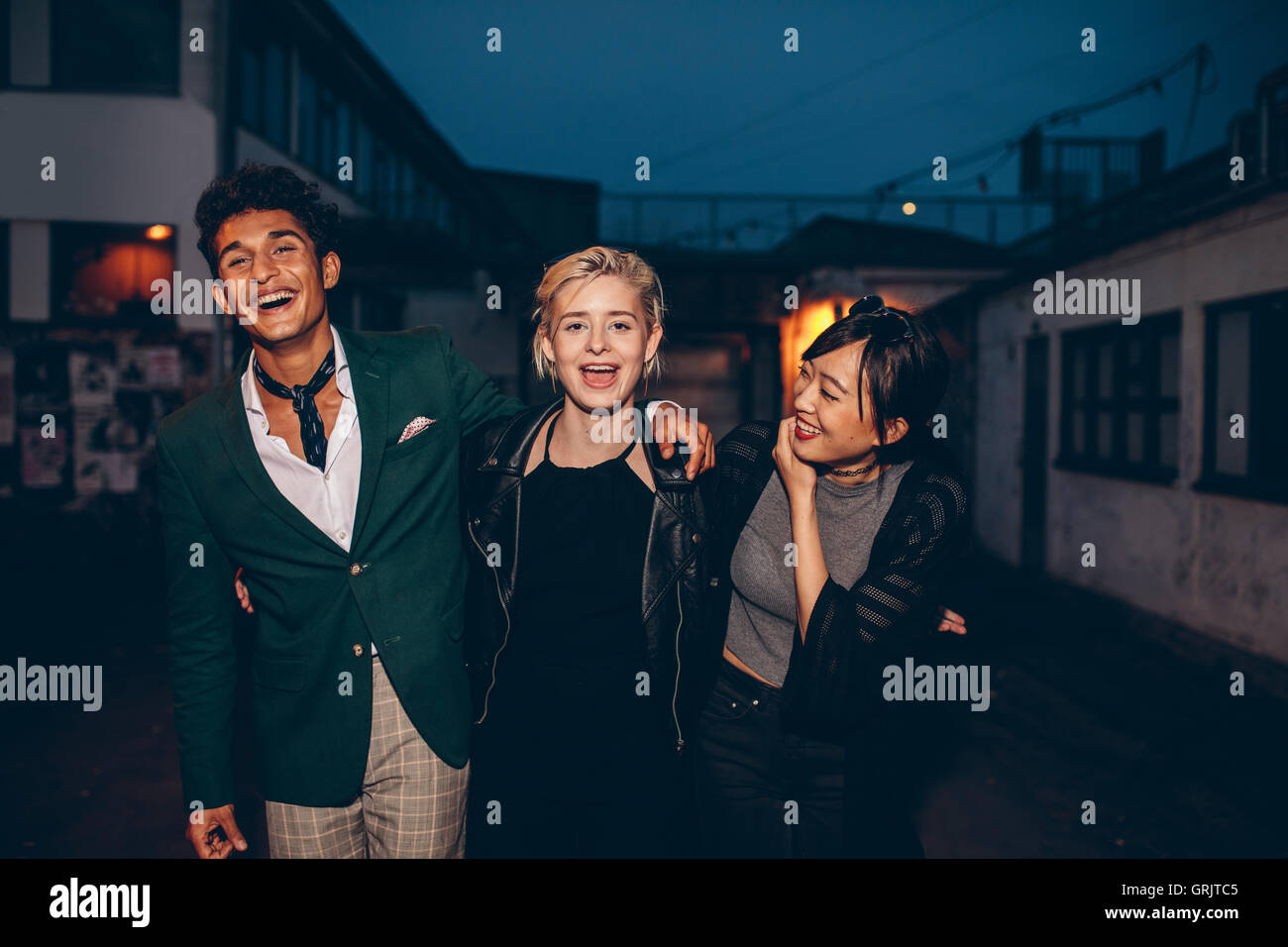Aufnahme des jungen Menschen zu Fuß auf der Stadtstraße in Abend und lachen. Drei junge Freunde, die Spaß am Stadtstraße in der Nacht. Stockfoto