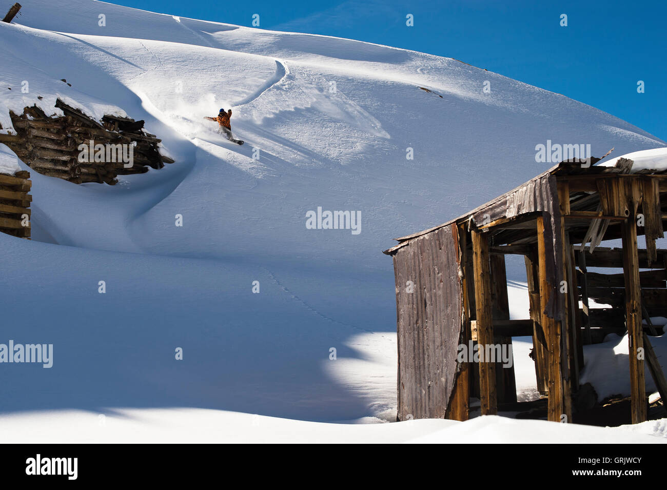Snowboarder einen Schrägstrich in Pulver zu tun, indem ein Bergbau-Altbau Stockfoto