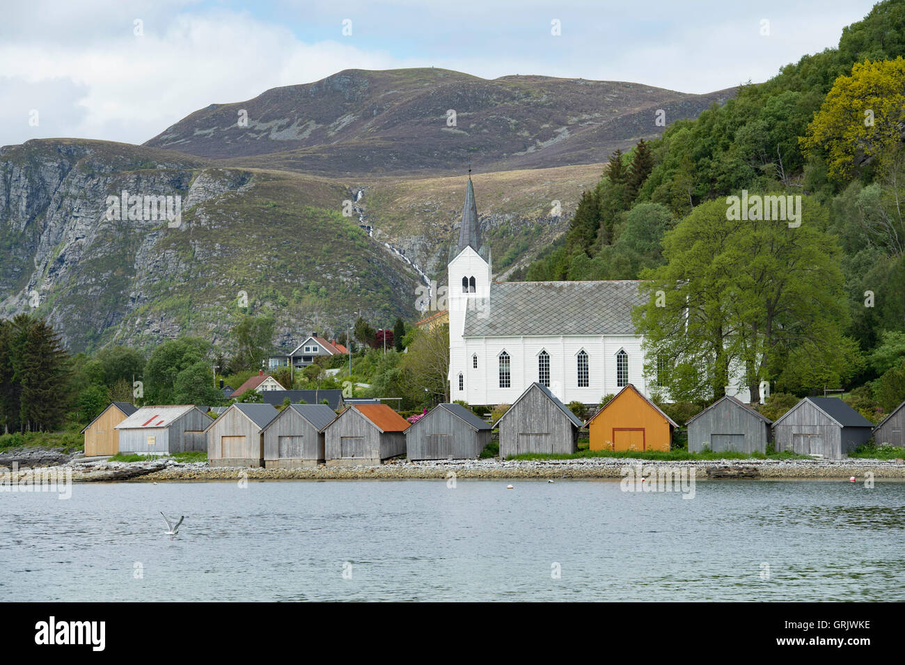 Eine Kirche in Selje Norwegen umgeben Bootshäuser mit einem Wasserfall im Hintergrund Stockfoto