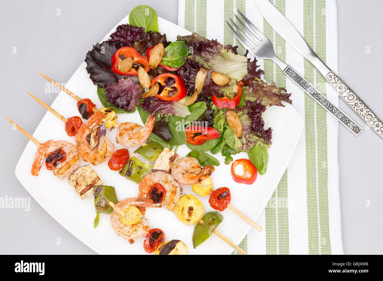 Portion leckere pikante Garnelen Spieße mit Paprika und Tomaten serviert mit einem Salat von frischem Blattgemüse, Overhead o anzeigen Stockfoto