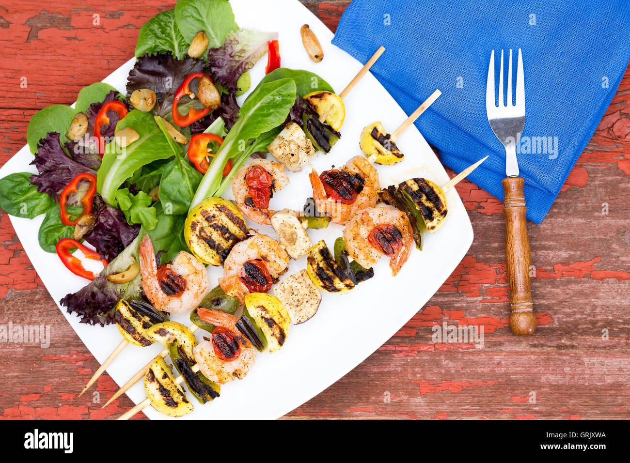 Drei Gourmet-Garnelen Spieße oder Kebabs mit grünem Salat, Tomaten und Paprika, niedrigen Winkel hautnah auf einem Tisch. Served w Stockfoto