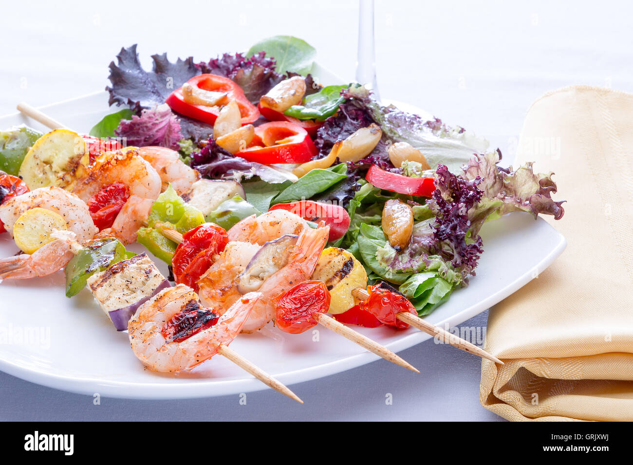 Garnelen-Spieße mit Paprika und Tomaten serviert mit einem frischen gemischten Salat für ein Abendessen mit köstlichen Meeresfrüchten, niedrigen Winkel hautnah Stockfoto