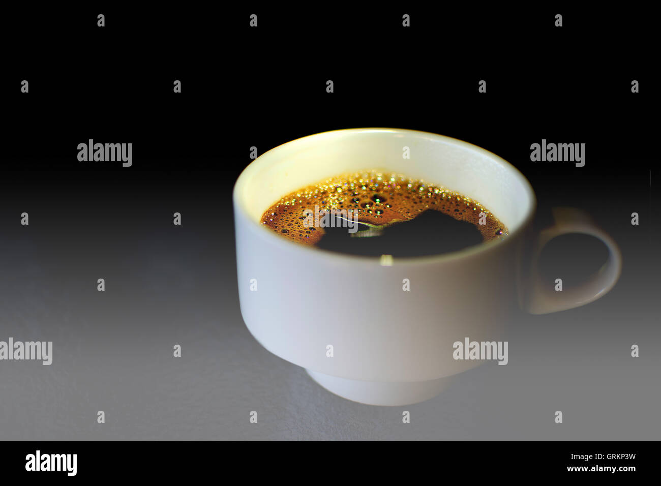 Kaffeetasse auf einem Glastisch. Weiße Kaffeetasse hautnah mit dunklem Hintergrund und dramatisches Licht. Stockfoto