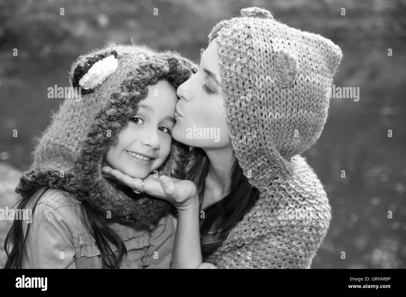 Mutter mit Tochter beide tragen Hoodies und warme Kleidung sitzen im freien umarmen glücklich, grünen Hintergrund, schwarz weiße edition Stockfoto