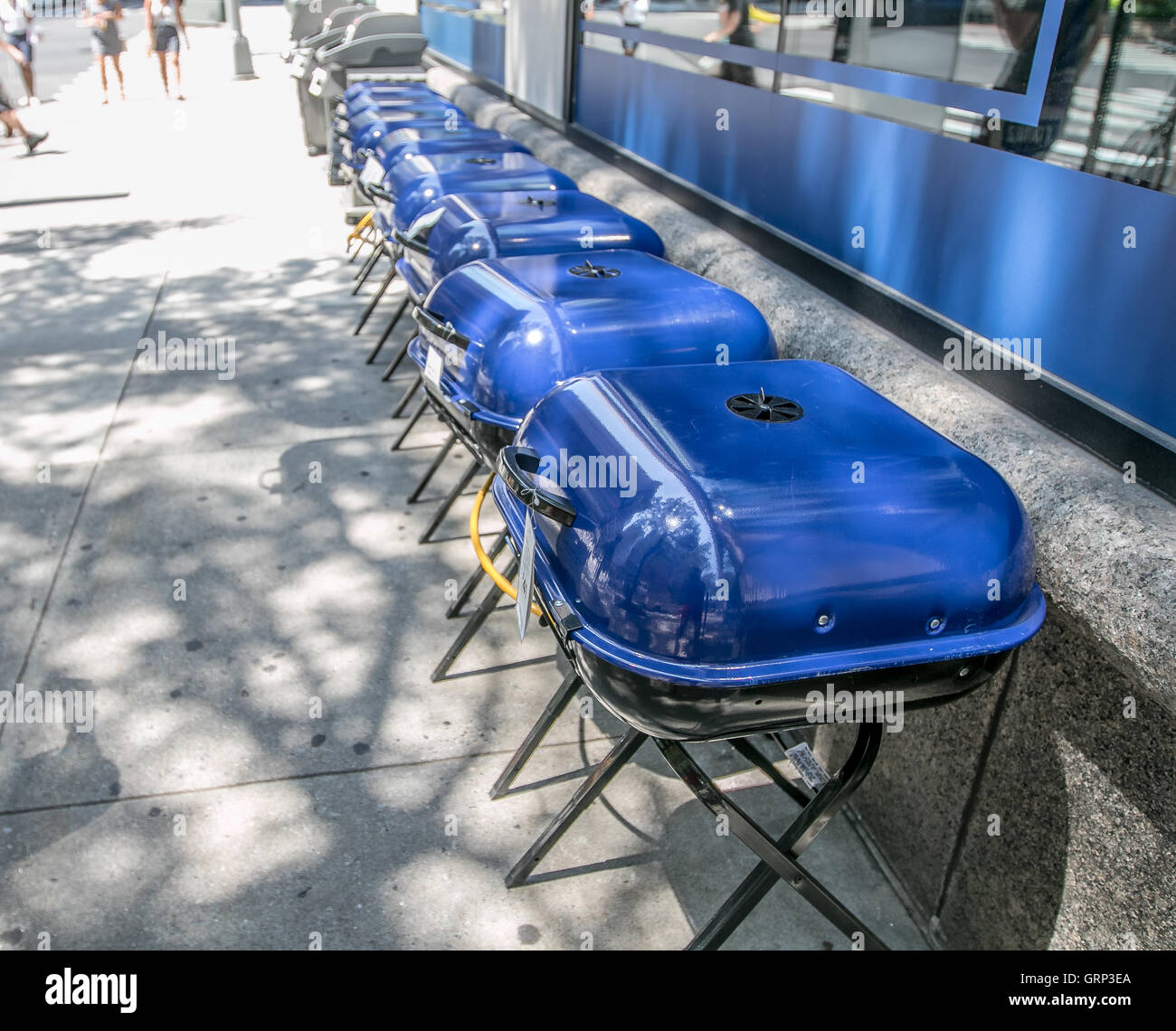 Eine Reihe von blauen Grillgeräte zum Verkauf ist von einem Geschäft an einem sonnigen Sommertag dargelegt. Stockfoto