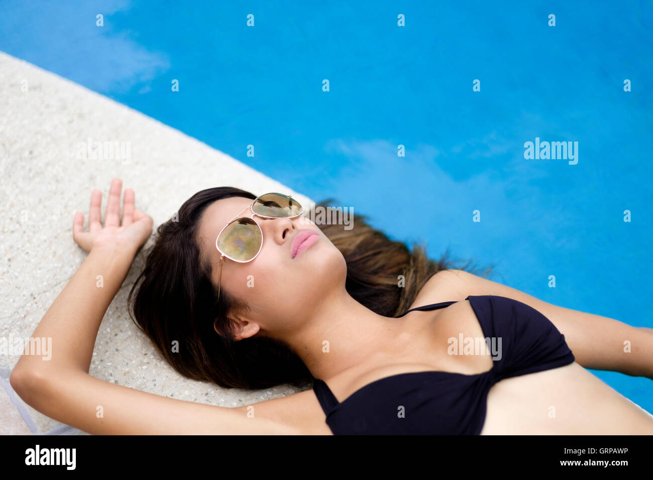 Junge Frau mit Sonnenbrille in Pilotenform Sonnenbaden am Pool mit geschlossenen Augen. Stockfoto