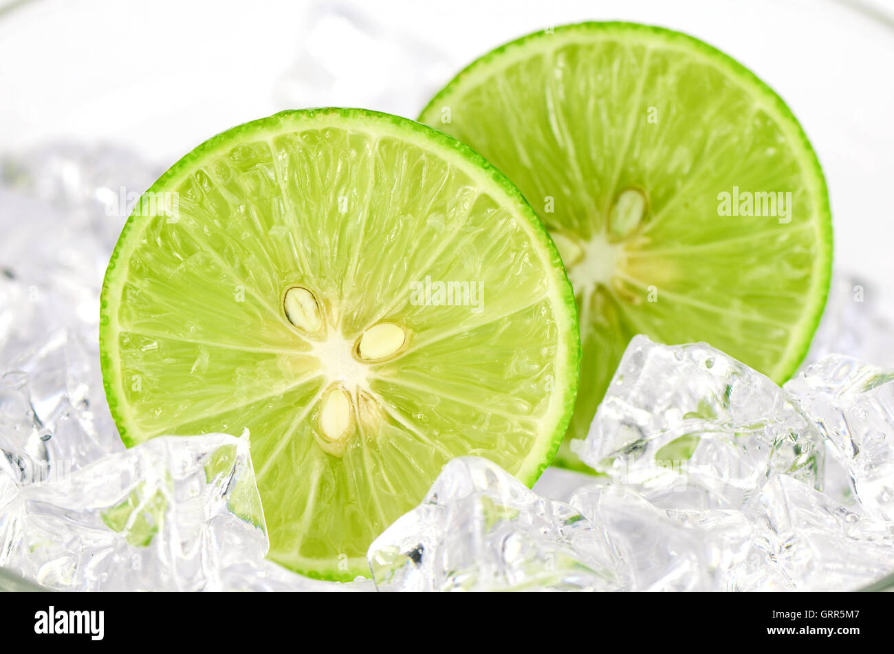 Geschnittene Limette (Citrus Aurantifolia (Christm.)  Swingle) und Eis auf weißem Hintergrund. Stockfoto