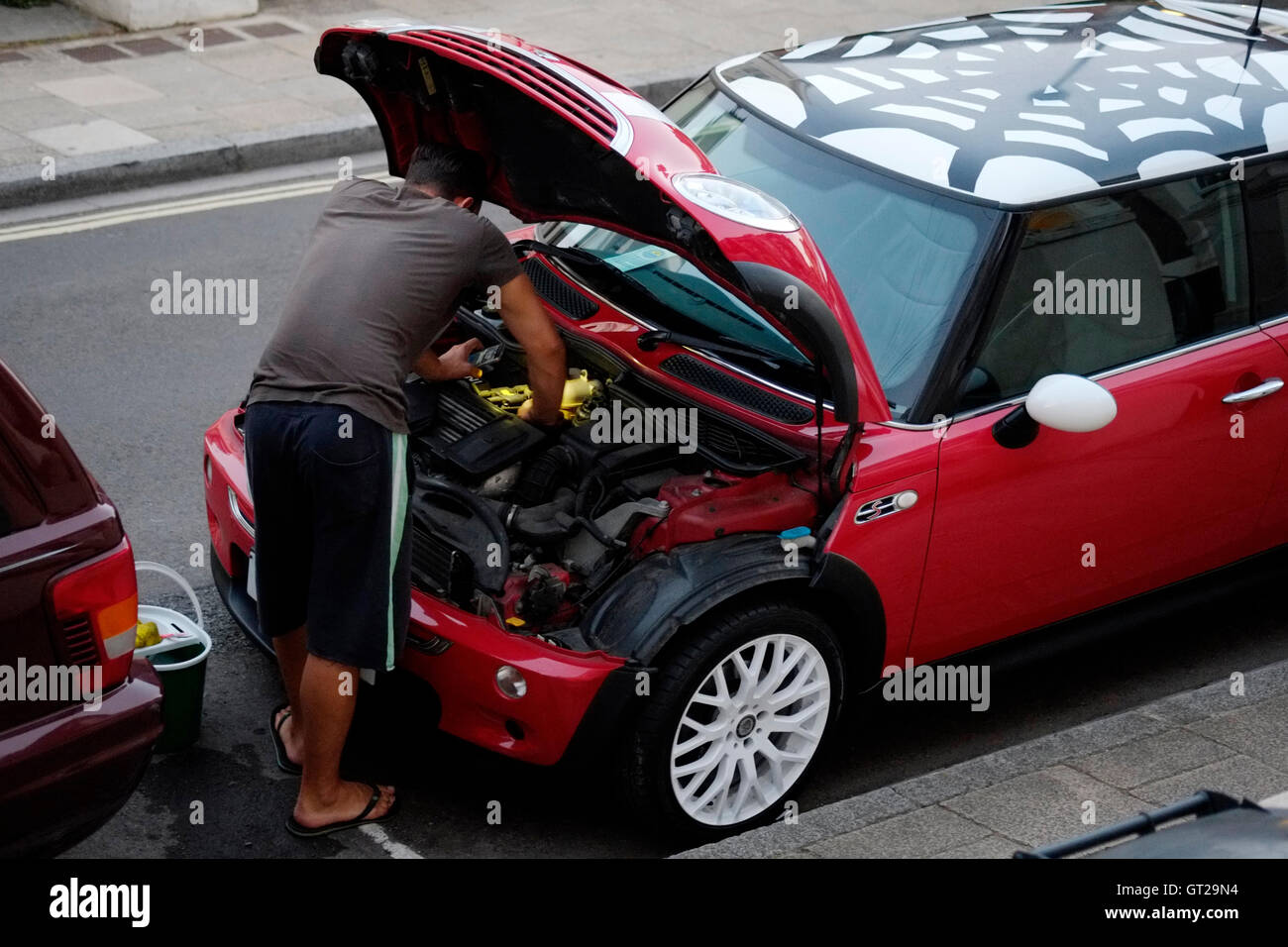 Mann Reinigung Auto Motorraum bei Einbruch der Dunkelheit mit Licht aus seinem Smart phone England uk Stockfoto