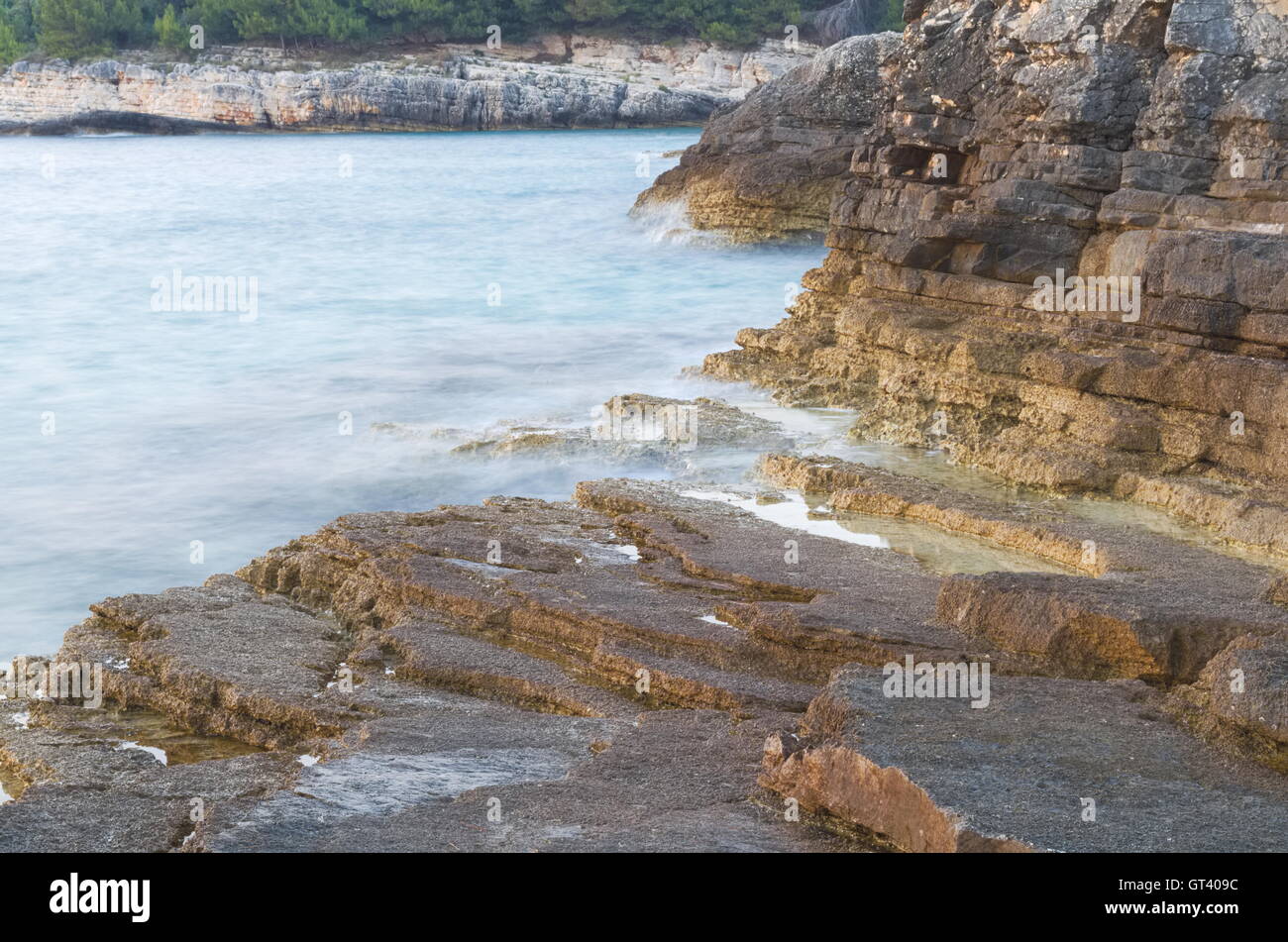 Blaue wellenförmige Meer und braune Felsenufer Langzeitbelichtung Stockfoto