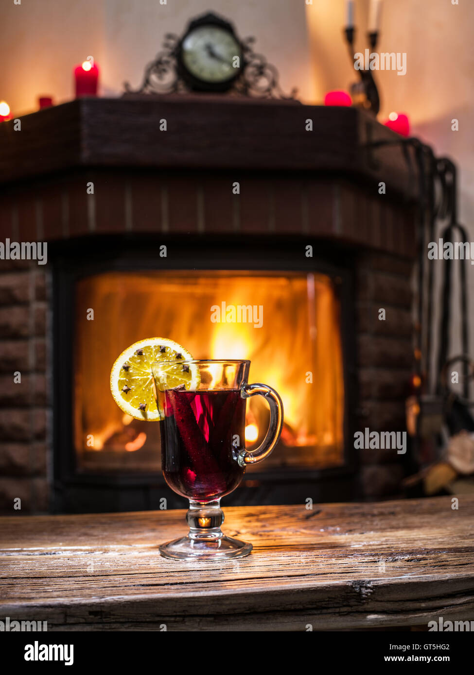 Glühwein mit Orangenscheibe, Nelken und Zimtstange. Kamin mit warmen Feuer im Hintergrund. Stockfoto