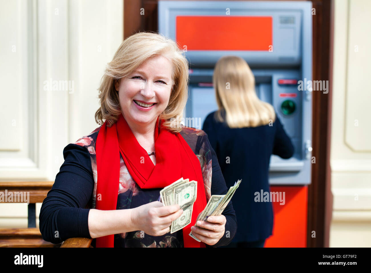 Reife blonde Frau Geldzählen in der Nähe von Geldautomaten im shop Stockfoto