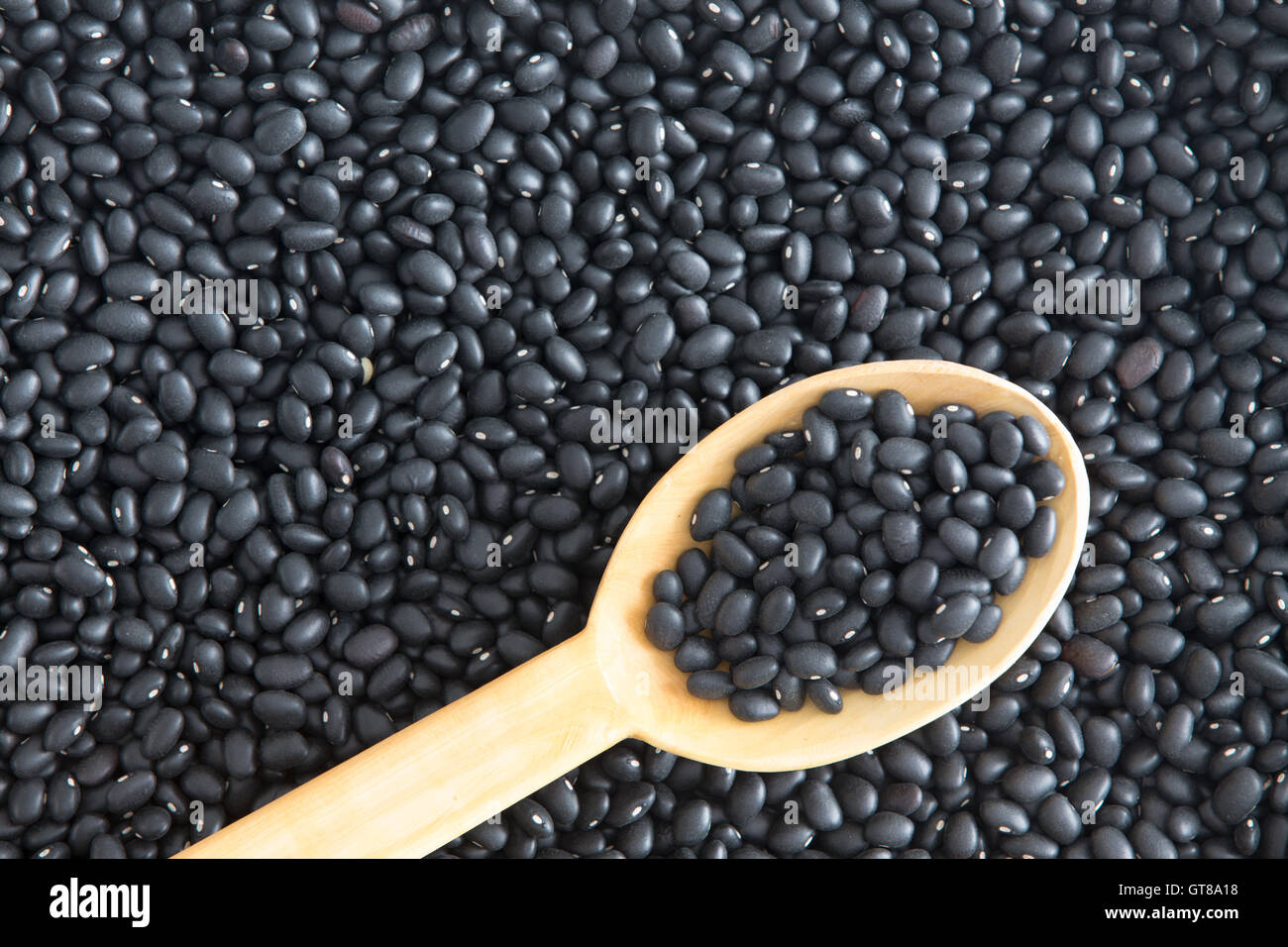 Background Textur gesunde schwarze Bohnen, Phaseolus Vulgaris, einer Vielzahl von Kidney-Bohnen mit einem rustikalen Holzküche Löffel liegen Stockfoto