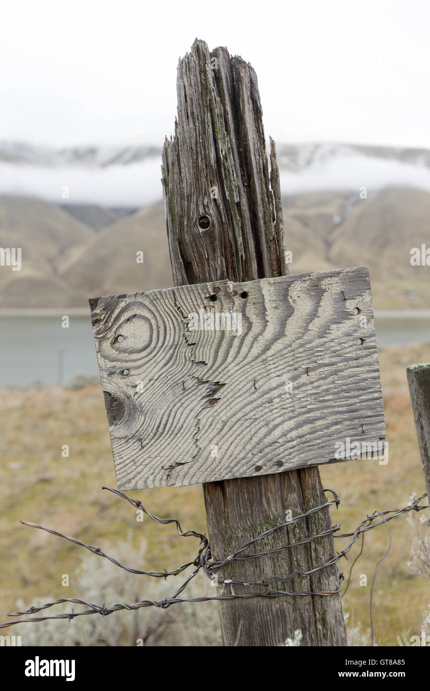 Alten Holzzaun Post mit Resten von Stacheldraht Zaun Draht und einem rustikalen leer Holz Schild mit ein interessantes Muster der Maserung des Holzes Stockfoto