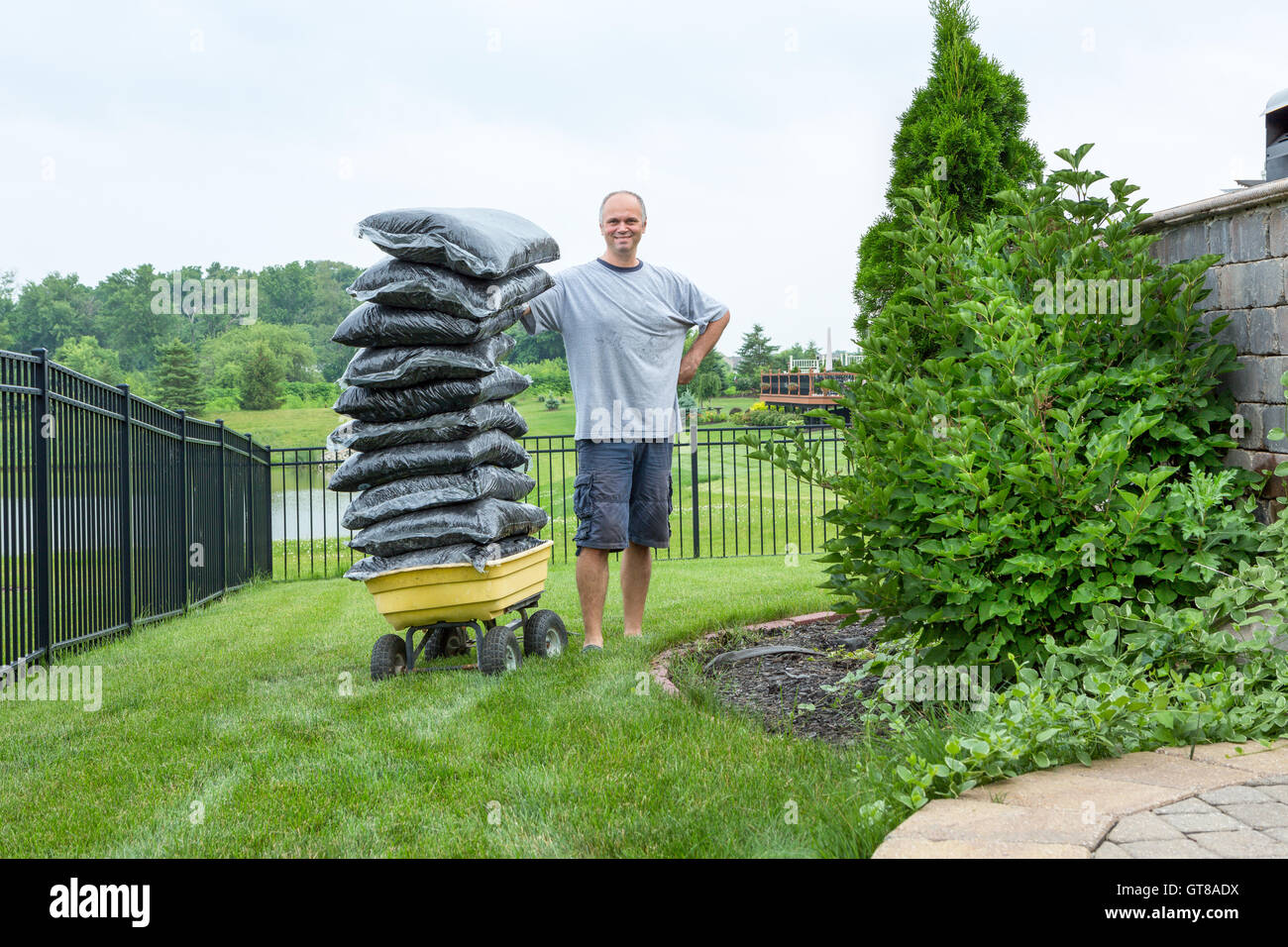 Hausbesitzer Mann stehend neben einem Garten Wagen mit einem Stapel von Säcken Mulch im Garten beim Betrachten der Kameras. Stockfoto