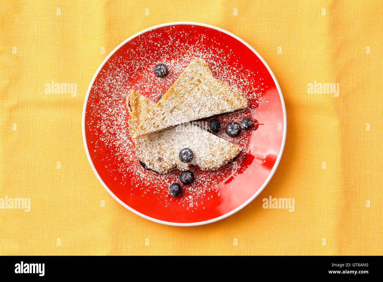 Luftaufnahme von einem leckeren französischen Toastbrot mit Erdbeere Konfitüre auf runde rote Platte mit Heidelbeeren Früchten füllen. Isoliert auf Yell Stockfoto