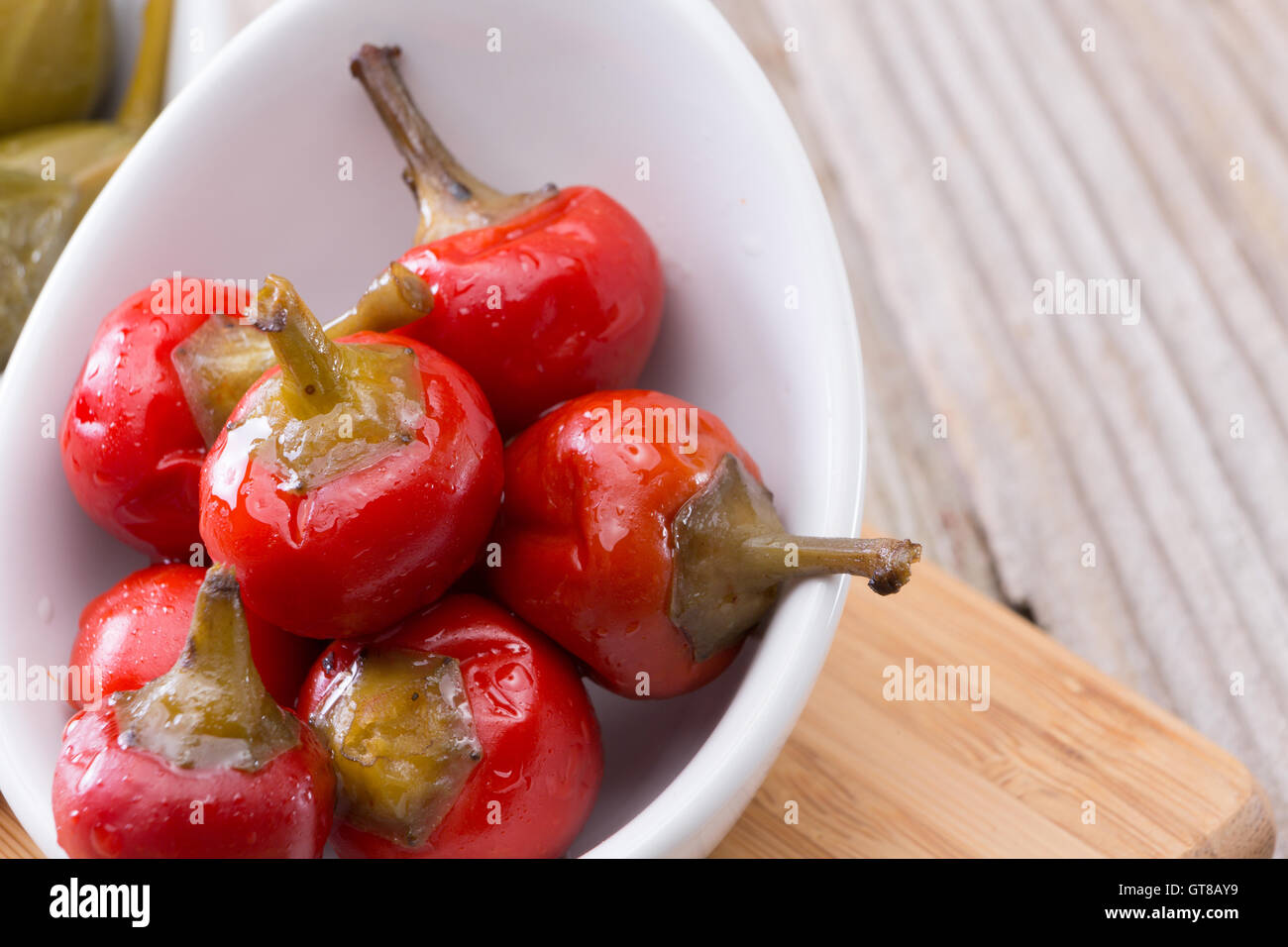 Frische rote Piment oder Cherry Pfeffer auf weiße Schüssel auf einem Holztisch in der Küche hautnah. Stockfoto