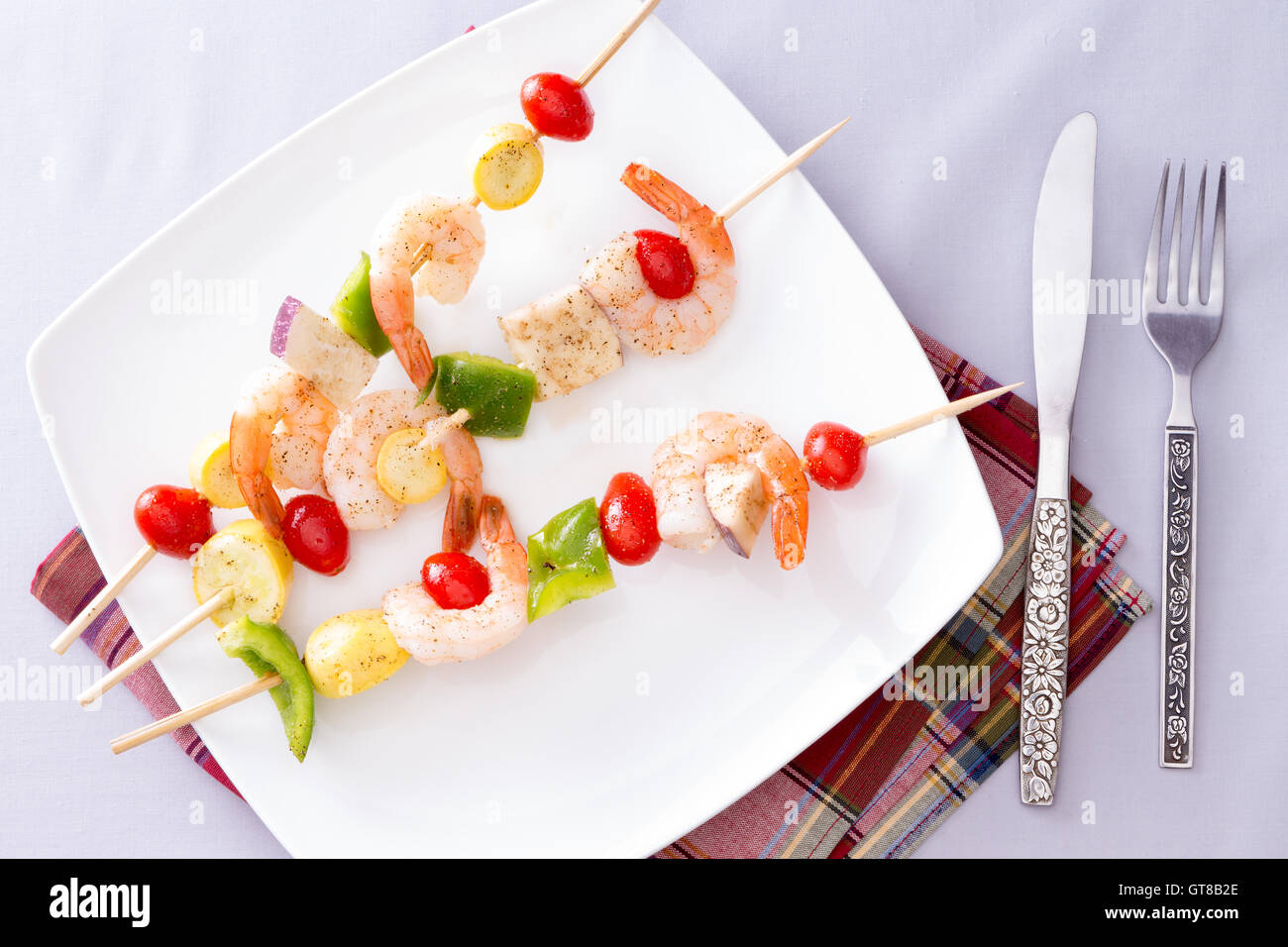 Drei leckere Gourmet-Garnelen Spieße oder Kebabs auf weißem Teller auf einem weißen Tisch mit Servietten und Besteck, eingefangen in hoch ein Stockfoto