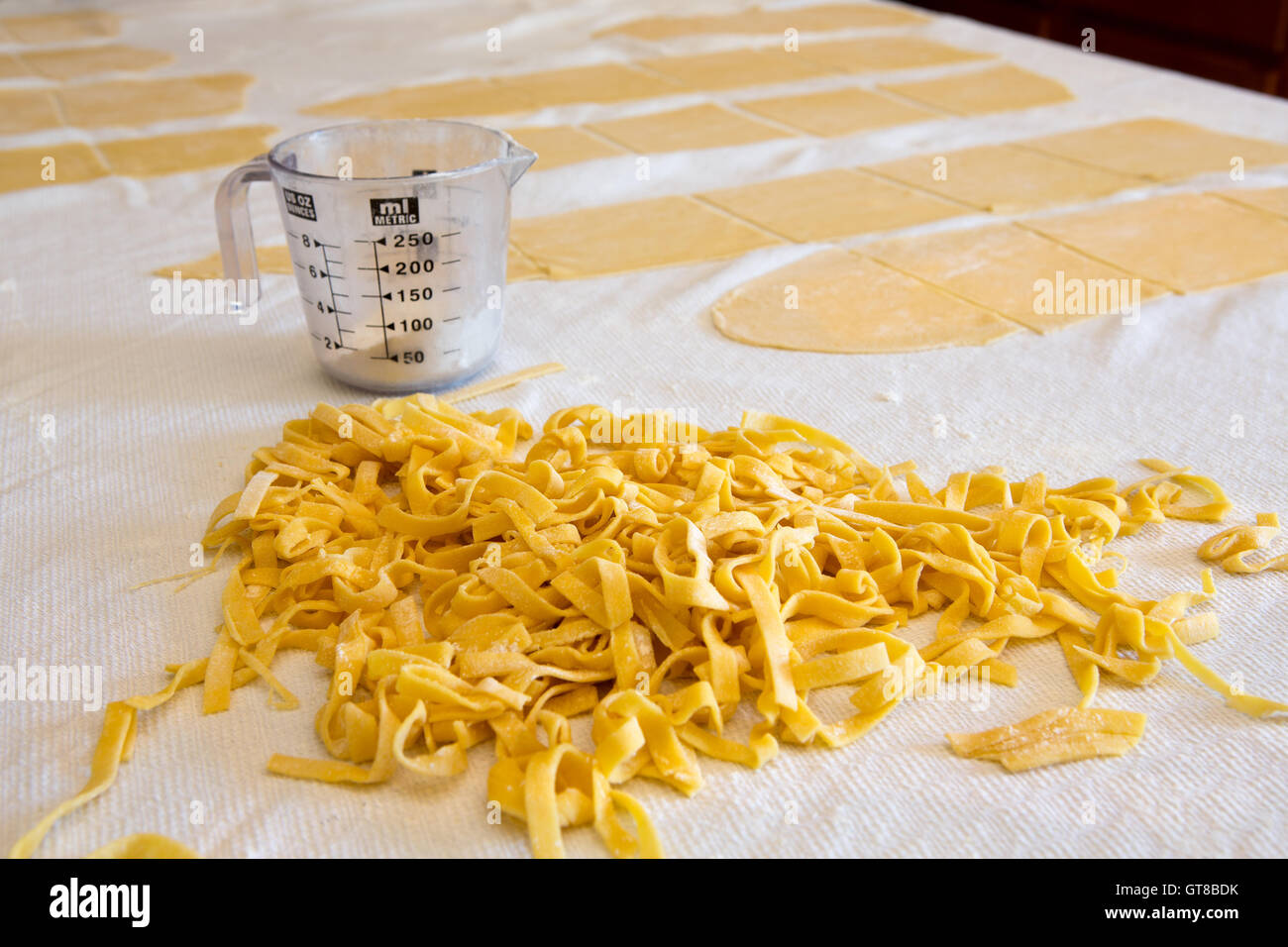 Haufen von frischen hausgemachten Bandnudeln Nudeln zubereitet mit Grieß und Hartweizen Weizen-Teig auf einer Küchenarbeitsplatte mit Blättern von unbeschnittenen d Stockfoto